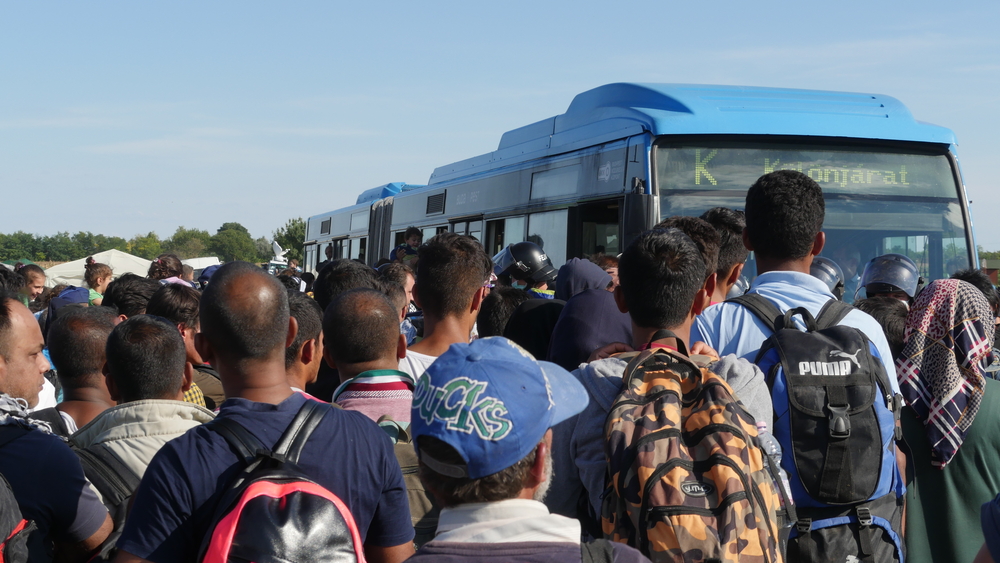 Refugees wait to board a bus at a migrant collection camp in Roszke, Hungary